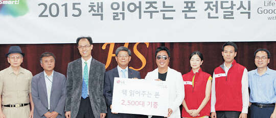 LG전자가 시각장애인용 스마트폰인 '책 읽어주는 폰' 신제품을 개발해 연말까지 시각장애인 2500명에게 순차적으로 기증한다고 25일 밝혔다. 지난 24일 오후 서울 강남구 개포동 하상장애인복지관에서 개최한 '책 읽어주는 폰' 전달식에 참석한 이충학 LG전자 경영지원부문장 부사장(왼쪽 네번째)과 가수 겸 배우 이동우씨(1급 시각장애, 다섯번째) 등이 기념촬영을 하고 있다.    LG전자 제공